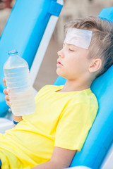 Little boy on the beach with a sunstroke holds a bottle of water