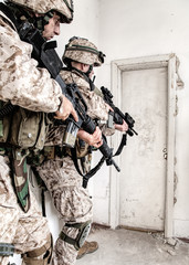 Fototapeta premium Marine assault team, counter-terrorism squad members, commando fighters in body armor, armed with service rifles, stalking through corridor to closed door, clearing rooms in abandoned city building