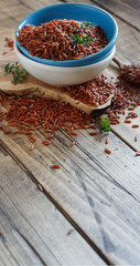 Uncooked Red rice in a bowl with a wooden spoon