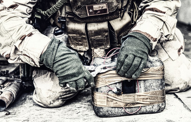 Army soldier, anti terrorist team combat engineer, ammunition technical officer, explosives military expert using pliers to cut wire on improvised explosive device, neutralizing homemade bomb on floor