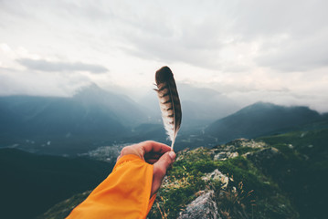Traveler hand holding bird feather moody mountains landscape aerial view Travel adventure lifestyle...