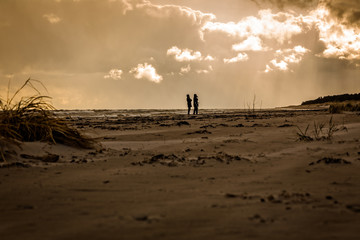 Man och kvinna promenerar p&aring; en kall och bl&aring;sig strand