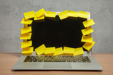 Laptop in reminders with yellow stickers notes on the display frame on table with gray wall