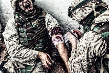 Marine wounded in shoulder, suffering of pain and screaming while receiving medical aid from...