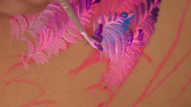 Art designer is drawing traditional ornament on the skin. She smears colorful lines.