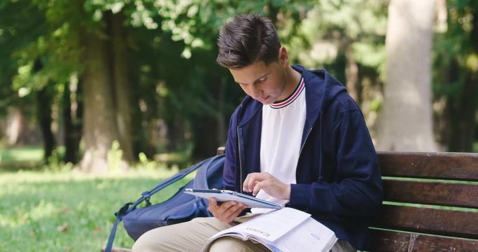 A student sitting on a bench uses the tablet to study , surf on social networks and stay in touch with their friends.