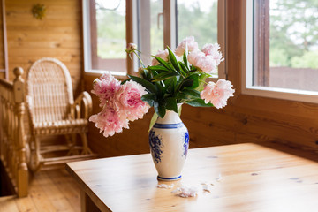 A bouquet of spring peonies in a vase on a table on a cozy terrace.