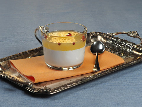 A cup of panna cotta with orange jelly and pink peppercorns set on a silver tray