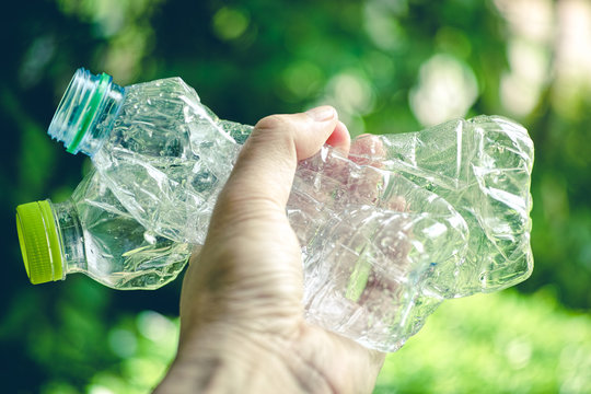 close up of hand holding used crashed plastic bottle for recycling