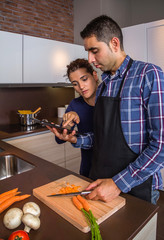 Young couple in home kitchen preparing food and looking recipe in a electronic tablet. Modern family lifestyle concept.