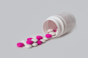 White and white tablets scatter from the white plastic bottle. Side view.