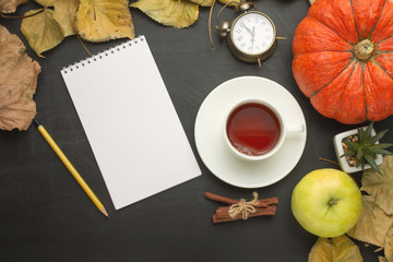 Tea with cinnamon and an alarm clock, a pumpkin and autumn foliage. flat lay season food items top view