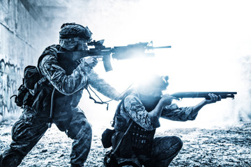 Silhouettes of two army soldiers, U.S. marines team in action, surrounded fire and smoke, shooting...