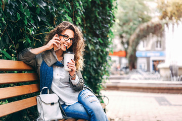 girl with curly hair drink coffee and use smartphone outdoor