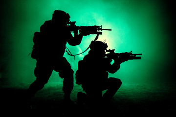 Fototapeta na wymiar Silhouettes of two army soldiers, U.S. marines team in action, surrounded fire and smoke, shooting with assault rifle and machine gun, attacking enemy with suppressive gunfire during offensive mission