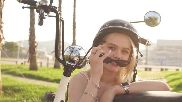 Close-up happy woman in seductive summer closing, helm, sunglasses sitting on electrocycle on stony sidewalk in urban palm parkside. Healthy lifestyle, Tourism and vacations.