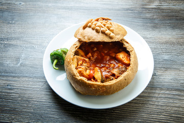 fish soup in original homemade brown bread bowl on white plate with green pepper