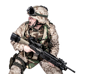 Studio shoot of modern infantry soldier, U.S. marine rifleman in combat uniform, helmet and body armor, screaming and crouching down with assault service rifle in hands isolated on white background