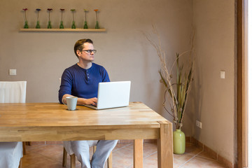 Mann schaut nachdenklich aus dem Fenster während er am Notebook arbeitet