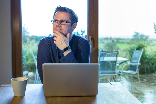 Digitaler Nomade sitzt nachdenklich vor seinem Notebook, w&auml;hrend es Draussen regnet
