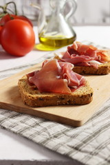 Spanish ham (jamon) on a piece of toasted whole grain bread, tomatoes and olive oil beside