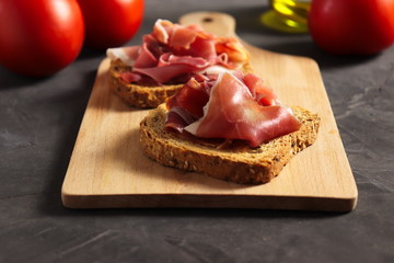 Spanish ham (jamon) on a piece of toasted whole grain bread, tomatoes and olive oil beside