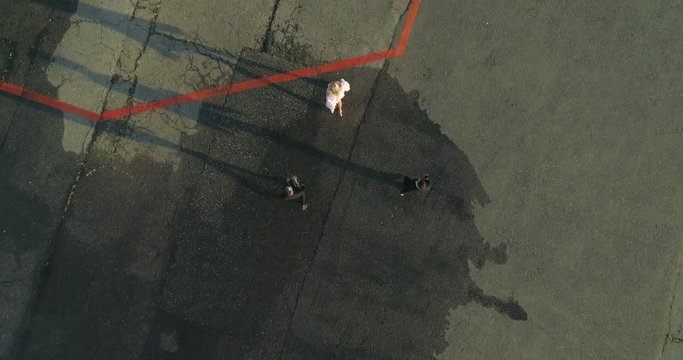 Cinematic frame of guards in black jackets accompany a beautiful girl to a private helicopter on the landing site. View from above.