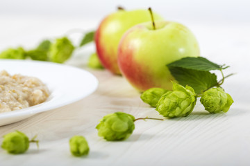 oatmeal porridge abundantly poured creamy melted butter on a white plate among apples and hops