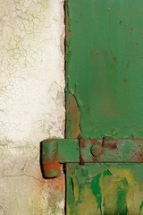 Old door hinge. Fragment of old wooden door of green color and a white wall affected by old age and rust.