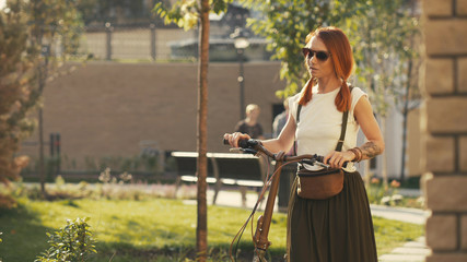 Woman walking beside riding bicycle on city park. Woman bike park