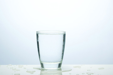 Glass of water with ice on the table and water drop of ice around glass.