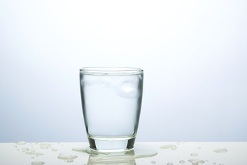 Glass of water with ice on the table and water drop of ice around glass.