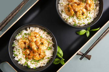 Two bowls of black color with rice and fried shrimp on a blue table. Asian food.