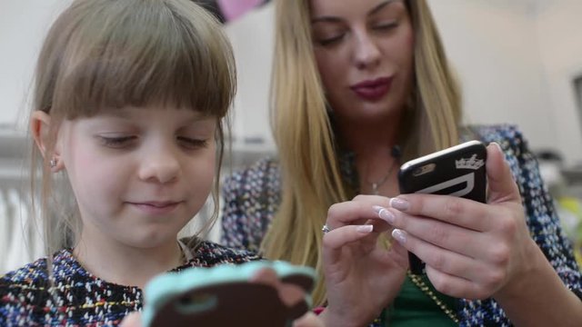 Mom and Daughter with Smartphones and Mobile phone shating in clothes store