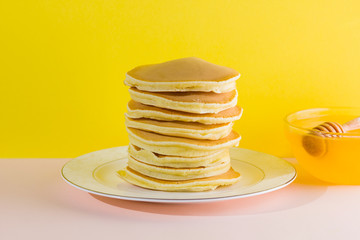 Pancakes with honey on a yellow pink background. Appetizing pancakes on a white plate and honey. Delicious dish for breakfast in the style of pop art