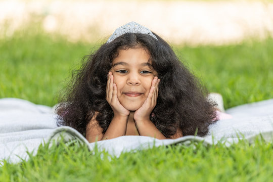 A young girl holding her head is laying on the green grass