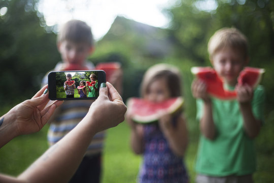Female hands taking photo of cheerful happy children eating watermelon
