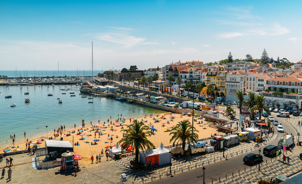 High vantage point of crowded sandy Praia do Ribeiro and boats on bay a a sunny summer day. Cascais is a small quaint village 30km west of Lisbon