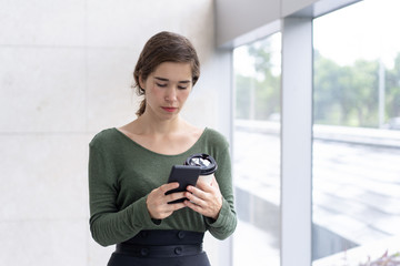 Portrait of concentrated female student texting message on phone. Young Caucasian businesswoman...