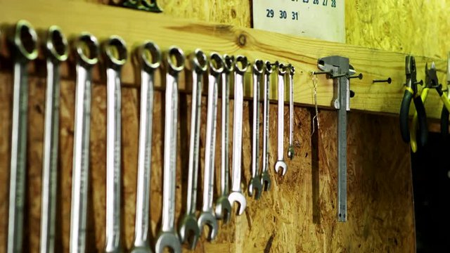 Human hand takes vernier caliper from wall. Set of mechanical tools in garage. Hand of car mechanic in auto repair service. Row of wrenches, measuring tool and equipment hangs on wall. Vintage garage