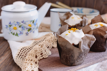 Freshly baked muffins in a paper wrapper are ready for eating, and next to a country style white teapot and a cup