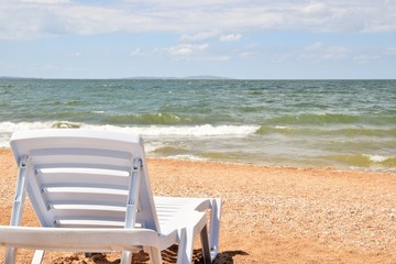 Отдых на море. Пустой шезлонг на пляже у кромки моря