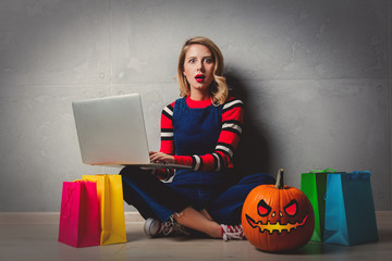 Portrait of a young style blonde girl in red striped sweater with notebook and pumpkin on grey...