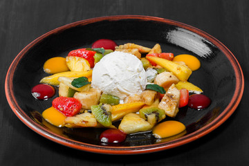 Fruit salad with banana, kiwi, orange, grapefruit in pineapple on plate over dark background. Healthy breakfast.