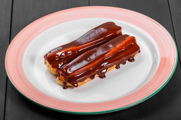 Chocolate eclairs on plate over dark wooden background, sweet food