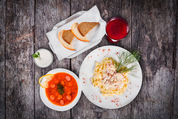 Delicious dinner table with Fettuccine pasta with meat, hot soup with sausages, bread and compote on wooden background. Top view