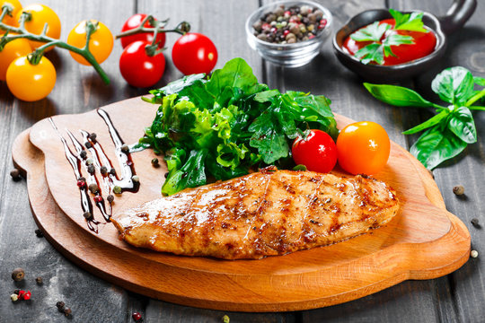 Grilled chicken fillet with fresh vegetable salad, tomatoes and sauce on wooden cutting board. Hot Meat Dishes. Top view