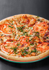 Pizza with chicken, tomatoes, mushrooms, greens and cheese on dark wooden background. Homemade pizza. Top view