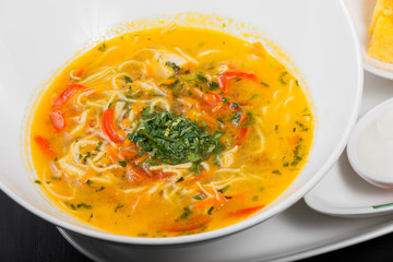 Vegetable soup, broth with noodles, herbs, parsley and vegetables in bowl on wooden black background, healthy food. Top view