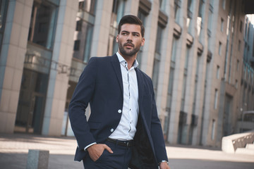 Confident businessman. Confident young man in full suit adjusting his sleeve and looking away while standing outdoors with cityscape in the background